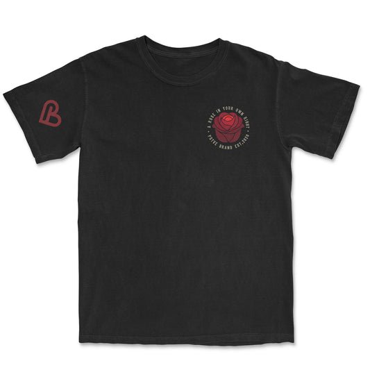 Black t-shirt with a red rose graphic on the left chest, encircled by the text "A ROSE IN YOUR OWN RIGHT - PSTVE BRAND EST. 2020". A red "B" logo is on the left sleeve.