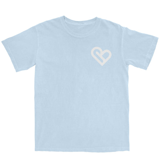 A light blue t-shirt with a white PSTVE (Positive) Brand logo on the left chest is displayed against a white background. The t-shirt has short sleeves and a round neckline.