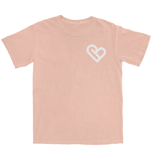 A light peach t-shirt with a white PSTVE (Positive) Brand logo on the left chest is displayed against a white background. The t-shirt has short sleeves and a round neckline.