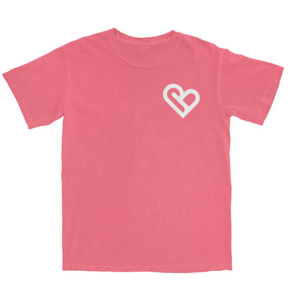 A coral-colored t-shirt with a white PSTVE (Positive) Brand logo on the left chest is displayed against a white background. The t-shirt has short sleeves and a round neckline.