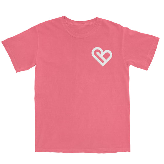 A coral-colored t-shirt with a white PSTVE (Positive) Brand logo on the left chest is displayed against a white background. The t-shirt has short sleeves and a round neckline.